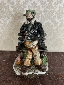 Porcelánová soška muže na lavičce s lahví vína